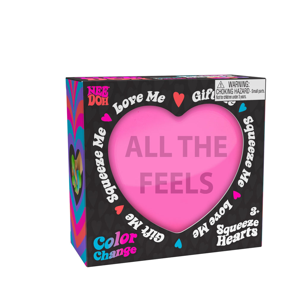 A boxed Nee Doh Color Change Squeeze Heart M9 toy. The packaging is predominantly black with colorful accents, featuring phrases like "ALL THE FEELS," "Squeeze Me," "Love Me," and "Gift Me." The box also includes a choking hazard warning for small parts.