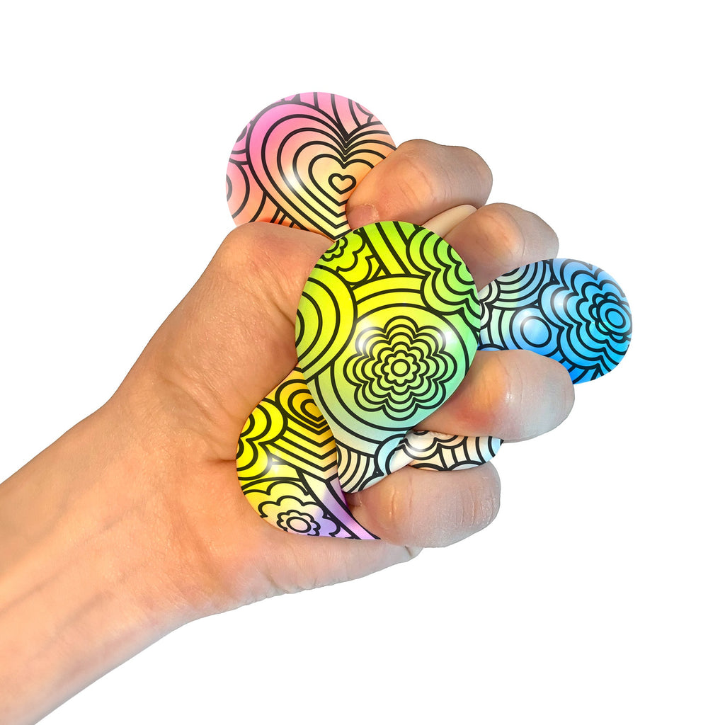 A hand squeezing a NeeDoh Press-Doh L6. The colorful doh is visible through the white and black designs of the exterior.